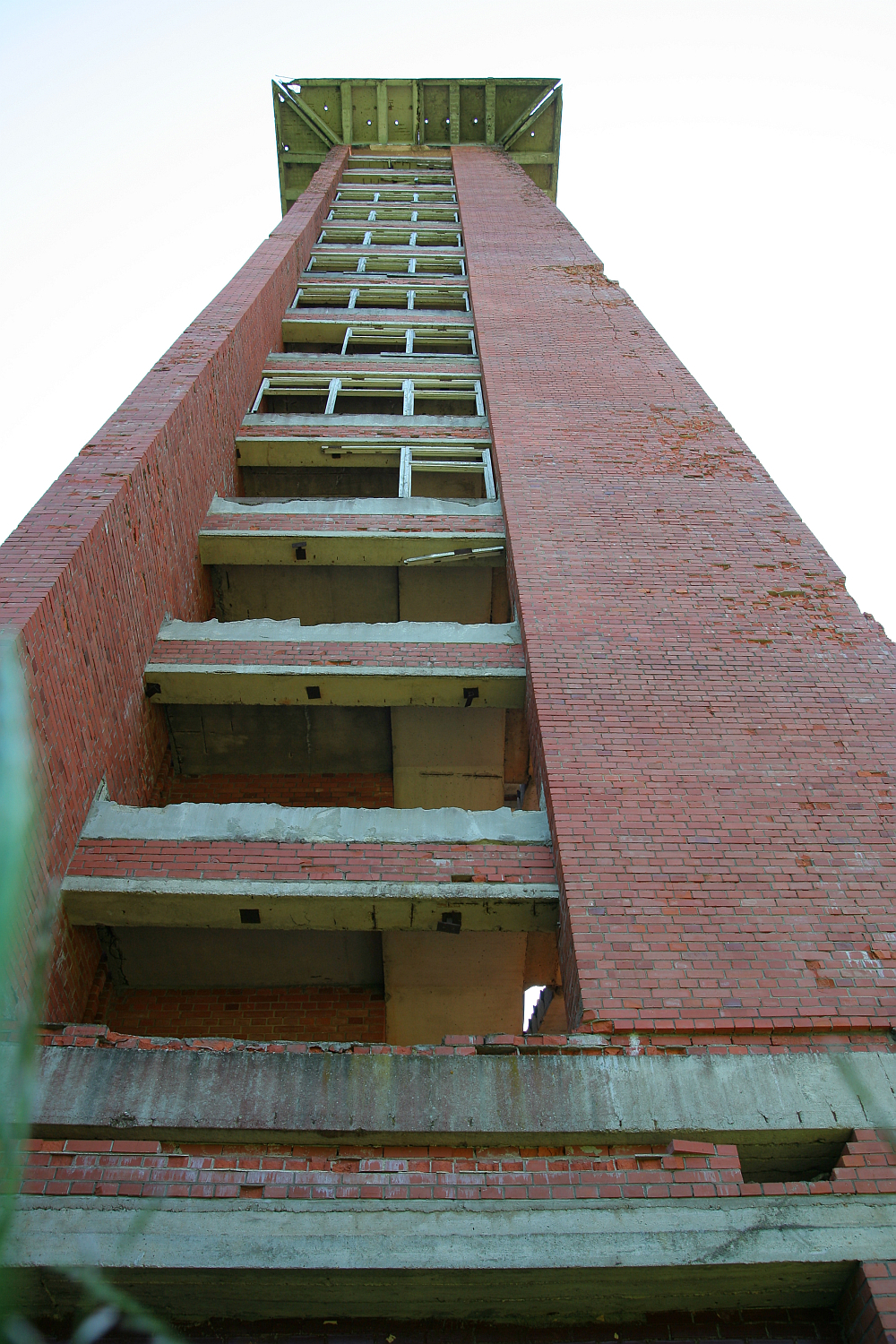A towering, abandoned red brick building stands desolate against a clear sky in Gaiziņš, with vacant window frames and no visible doors or glass, hinting at a bygone era.