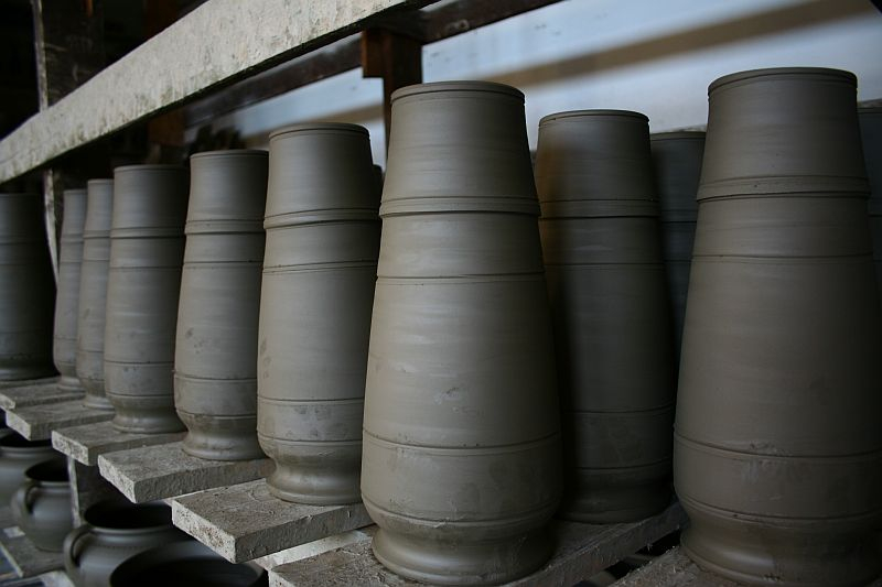 Freshly thrown clay pots lined up on a shelf in Romania, showcasing the uniformity and precision of a potter's craft before they are fired in the kiln.