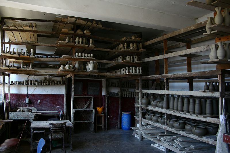 A rustic pottery workshop in Romania with shelves laden with unfinished clay vessels, pottery wheels, and tools, illuminated by soft natural light, evoking the quiet anticipation of creation.