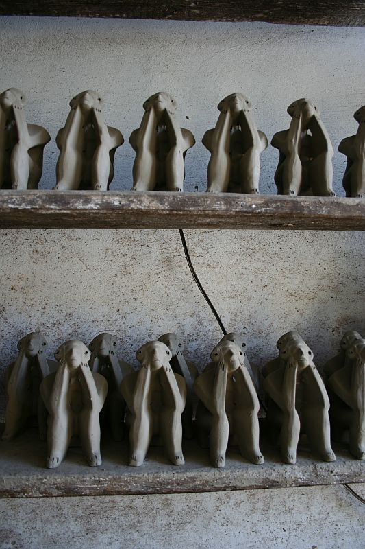 Rows of unfinished clay figures, resembling slim humanoid shapes with their heads in their hands, are placed neatly on wooden shelves in Romania, giving a sense of an art project in progress or a thematic display.