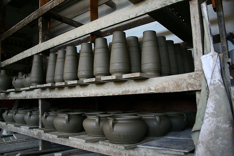 Shelves of pottery in various stages of completion, ranging from unfired clay vessels to pots ready for the kiln, showcasing the different steps in the ceramic making process in Romania.