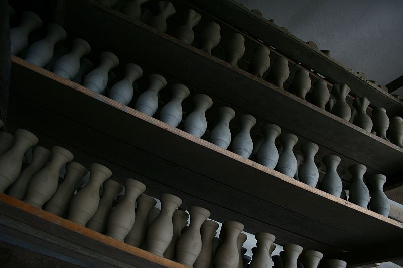 Rows of unfinished ceramic pottery pieces line wooden shelves inside a dark workshop in Romania, awaiting the next steps of their artisanal journey.