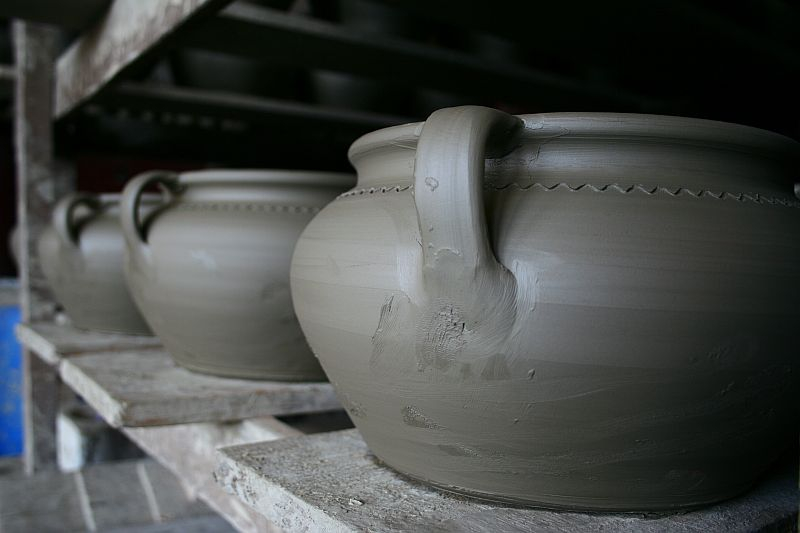 Freshly thrown clay pots with smooth surfaces and delicate decorative markings, reminiscent of traditional Romanian craftsmanship, sit on a shelf, awaiting the drying process before being fired in a kiln.