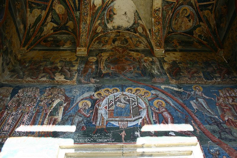 An ancient vaulted ceiling adorned with faded frescoes in Romania, depicting religious scenes with saintly figures and intricate patterns, showcasing Byzantine artistry in a state of elegant decay.