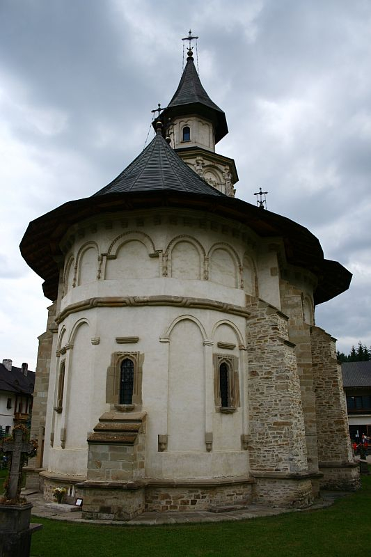 A historic stone church in Romania with a distinctive wooden bell tower and an octagonal apse under a cloudy sky, showcasing traditional architectural elements and cultural heritage.