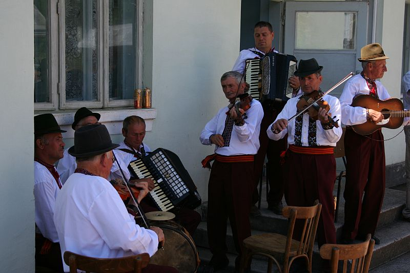 A traditional folk ensemble from Romania plays with passion, featuring an accordion, fiddle, and guitars, evoking the rich musical heritage of their culture in an outdoor setting.