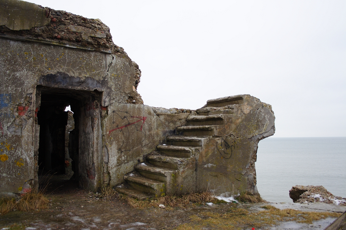 A dilapidated coastal Karosta WWII bunker with graffiti presents a staircase leading to nowhere, offering a poignant reminder of history's decay against the backdrop of a serene sea.