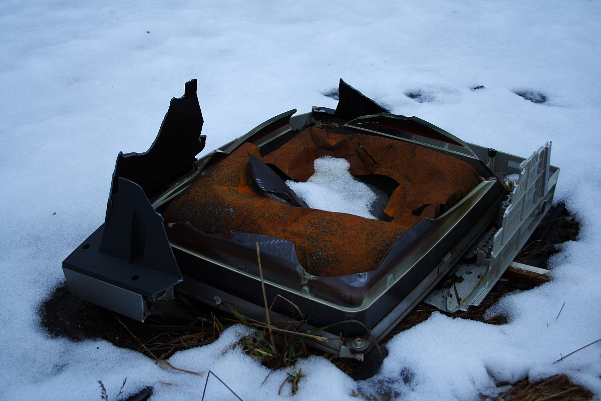A discarded, rusted television set lies broken on the snowy ground in Karosta, blending decay with the stillness of winter.