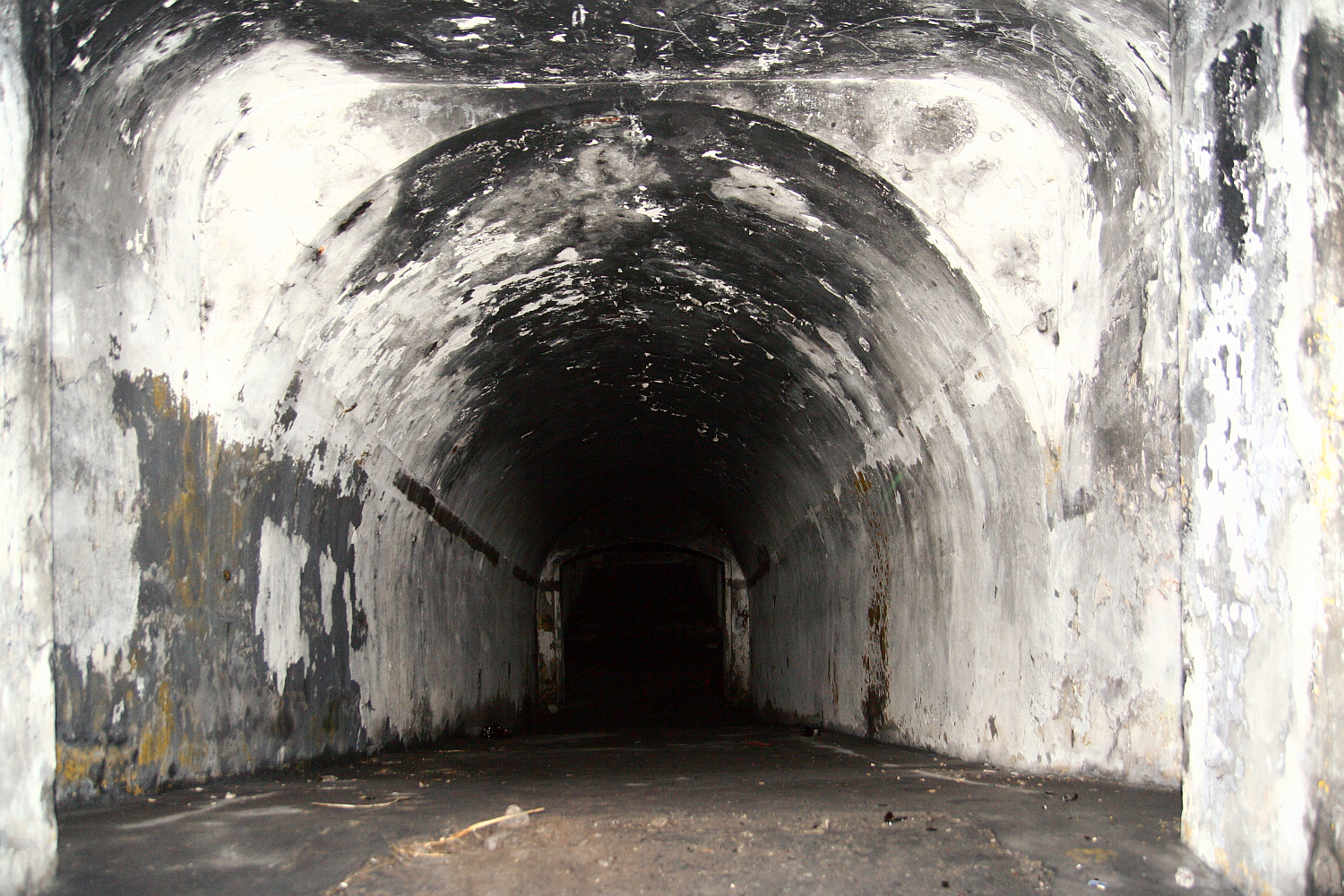 An abandoned, dark tunnel in Liepāja with peeling walls leading into an ominous void, suggesting decay and desolation.