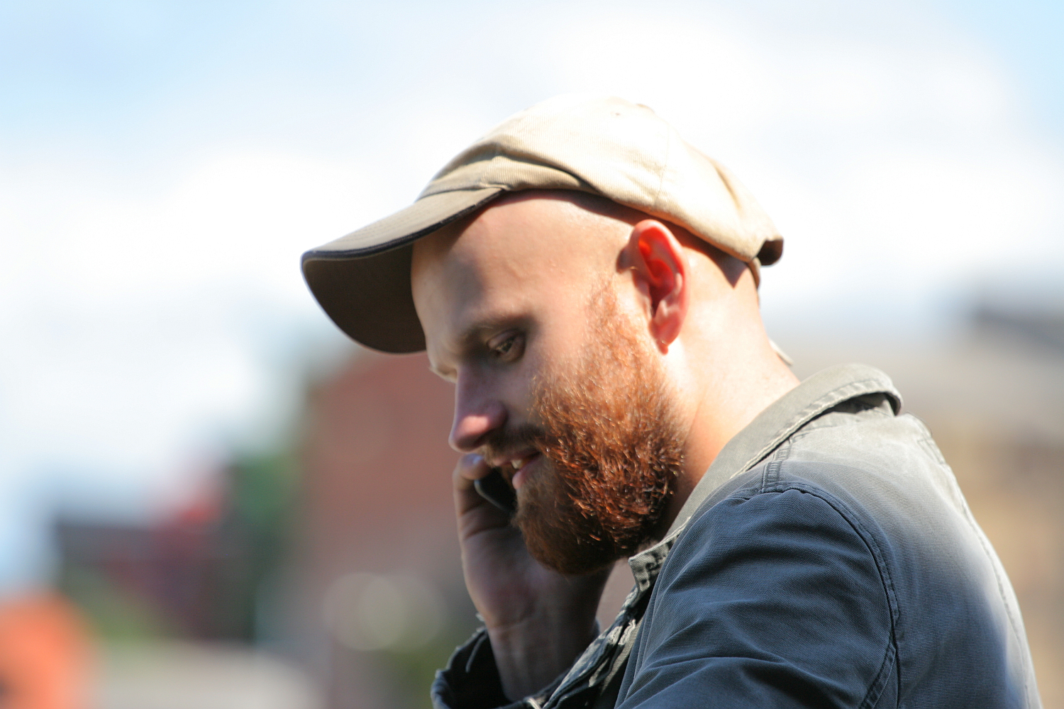 A bearded man in a flat cap is deep in thought, or perhaps conversation, as sunlight highlights his profile against a soft-focus background in Liepāja.