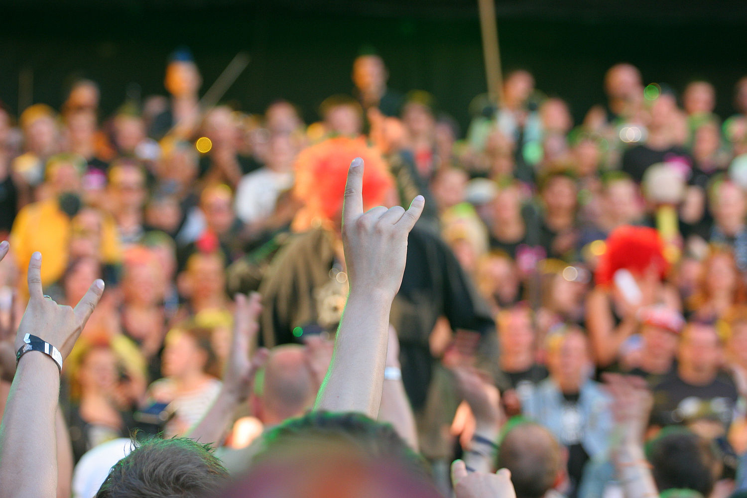 A large crowd at a punk concert, with a hand in the foreground making the "rock on" gesture. The audience is blurred in the background, and many are cheering or holding up their hands. The atmosphere is lively and energetic, reminiscent of a modern Laulupidu festival.