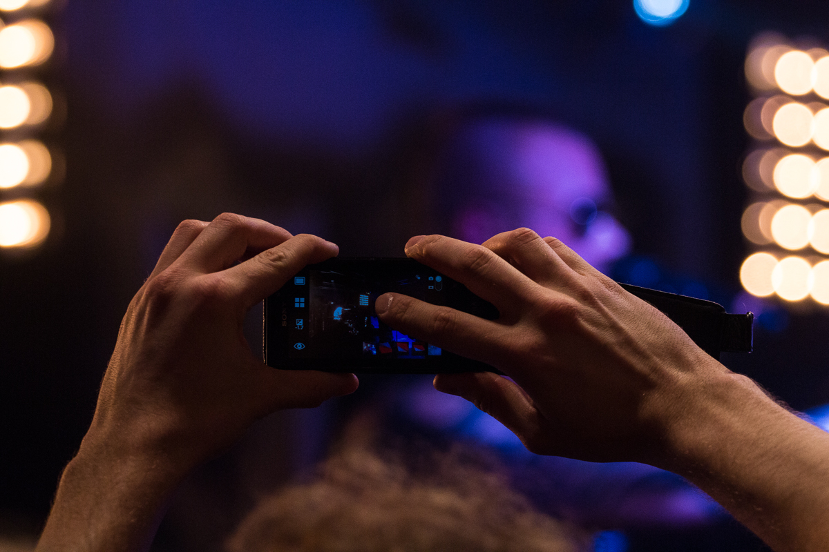 Close-up of a person’s hands holding a smartphone horizontally, capturing a photo or video of a blurred background with stage lights. The scene suggests a live performance by the Swedish heavy metal band Sabaton. The hands are well lit, while the background remains out of focus. via @atisgailis
