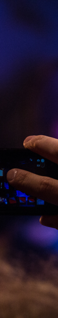 Close-up of a person's hands holding a smartphone horizontally, capturing a photo or video of a blurred background with stage lights. The scene suggests a live performance by the Swedish heavy metal band Sabaton. The hands are well lit, while the background remains out of focus.