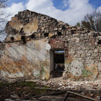 Ruins of an old stone structure in Daugavgrīva with weathered walls and a collapsed roof, surrounded by scattered debris and bare trees under a partly cloudy sky.