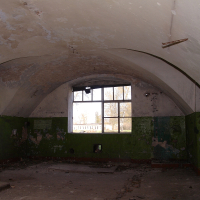 An abandoned room with a vaulted ceiling and peeling green paint, showcasing a large window that frames a view of Daugavgrīva, suggesting a haunting contrast between the decay inside and the