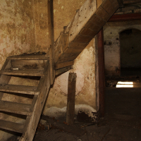 An old, decrepit staircase in a dilapidated room with peeling walls, suggesting a long-abandoned building in Daugavgrīva with a history lost to time.