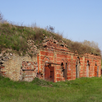 Ruined brick structure with arched doorways, partially reclaimed by nature, stands under a clear sky in Daugavgrīva, evoking a sense of history and decay amidst a green landscape