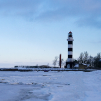 A frozen lake with a lighthouse in Daugavgrīva during winter.