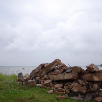 A pile of rubble foregrounds a tranquil lake under a cloudy sky, hinting at past construction or demolition amidst natural serenity, suggesting it's not possible to accurately determine the full history without more details