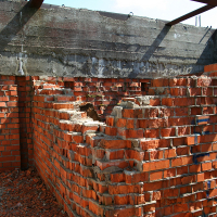 Unfinished and abandoned, the red brick structure stands in disrepair with a fragmented wall under a concrete ceiling on Gaiziņš, exposed to the elements and the relentless passage of time.