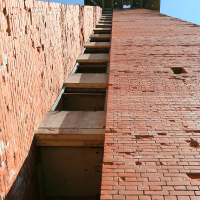 A towering view from the base of an imposing brick structure at Gaiziņš, showcasing a series of protruding concrete steps ascending to a platform under a clear blue sky.