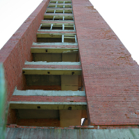 A towering, abandoned red brick building stands desolate against a clear sky in Gaiziņš, with vacant window frames and no visible doors or glass, hinting at a bygone era.