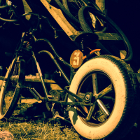 A worn-out bicycle with a large white tire rests against a wooden structure in a dimly lit outdoor setting, remnants of the 2013 festival. The bike appears old and rusted, with a license plate featuring the number 34. Various other bike parts are visible in the background, and hay covers the ground.