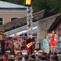 A group of people standing on a stage in front of a building during Dzelzs vilks ielīgo '09.