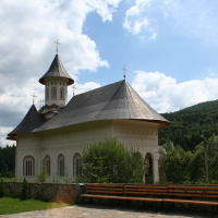 A picturesque church with a prominent bell tower and shingled roof, nestled in a serene green landscape of Romania, with fluffy clouds above and a welcoming bench at the forefront.