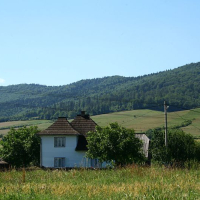Rural landscape in Romania with traditional houses against a backdrop of rolling, forest-covered hills under a clear blue sky.