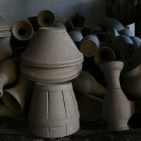 An assortment of unfinished clay pottery pieces, including pots and pitchers from Romania, set to dry, with prominent shadows casting a serene atmosphere over the traditional craft display.