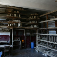 A rustic pottery workshop in Romania with shelves laden with unfinished clay vessels, pottery wheels, and tools, illuminated by soft natural light, evoking the quiet anticipation of creation.