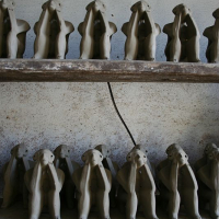 Rows of unfinished clay figures, resembling slim humanoid shapes with their heads in their hands, are placed neatly on wooden shelves in Romania, giving a sense of an art project in progress or a thematic display.