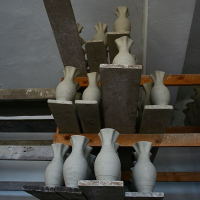 Unfinished ceramic vases at various stages of completion sit atop a wooden shelving unit in a Romanian pottery workshop, awaiting the next steps of their artistic transformation.