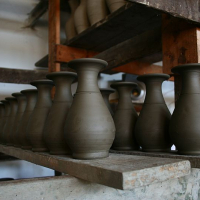A row of unfinished clay pots lines up on a wooden shelf in a potter's workshop in Romania, waiting to be fired and glazed.
