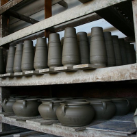 Shelves of pottery in various stages of completion, ranging from unfired clay vessels to pots ready for the kiln, showcasing the different steps in the ceramic making process in Romania.