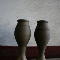 Two unfinished clay pots from Romania stand side by side against a white wall with a red baseboard, showcasing the symmetry and natural beauty of handcrafted pottery.