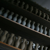 Rows of unfinished ceramic pottery pieces line wooden shelves inside a dark workshop in Romania, awaiting the next steps of their artisanal journey.