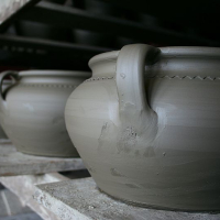 Freshly thrown clay pots with smooth surfaces and delicate decorative markings, reminiscent of traditional Romanian craftsmanship, sit on a shelf, awaiting the drying process before being fired in a kiln.