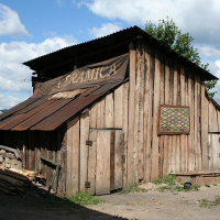 Rustic wooden shed with a corrugated iron roof appearing to sell drinks, adorned with a colorful geometric wall decoration, situated under a cloudy sky in Romania, with stacks of wood and residential buildings