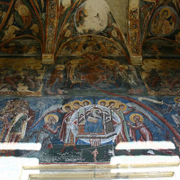 An ancient vaulted ceiling adorned with faded frescoes in Romania, depicting religious scenes with saintly figures and intricate patterns, showcasing Byzantine artistry in a state of elegant decay.