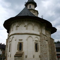 A historic stone church in Romania with a distinctive wooden bell tower and an octagonal apse under a cloudy sky, showcasing traditional architectural elements and cultural heritage.