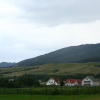 A serene Romanian countryside scene with rolling hills in the background, a cluster of houses in the foreground, and an overcast sky hinting at the possibility of rain.