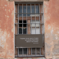 A weathered building facade with a barred window stands in the historic Daugavpils fortress. A black sign, mounted before the window, bears Rothko's quote: "There is no such thing as good painting about nothing." The peeling paint reveals patches of the underlying material, reminiscent of Latvian history.