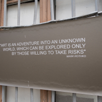 A large gray poster hangs on a weathered window of the fortress, displaying the quote: "Art is an adventure into an unknown world, which can be explored only by those willing to take risks." - Mark Rothko. This historical site in Daugavpils embraces the worn and adventurous spirit at its edges.