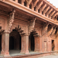The image shows a well-preserved, intricately carved, red sandstone structure with ornate arches and columns. Reflecting historical Indian design, it features detailed patterns and reliefs. The open courtyard and overhanging balconies add depth and richness to this testament of India's architectural heritage.