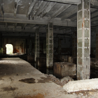 An Iļģuciems room in an abandoned building with concrete floors and pillars.