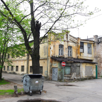An Iļģuciems building with a trash can in front of it.