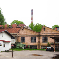 An old factory building in Iļģuciems with a car parked in front of it.