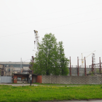 A green field in Iļģuciems next to a factory.